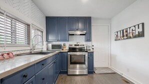 A kitchen with blue cabinets, stainless steel appliances, and a herringbone-patterned ceiling. - Walk to Downtown~3 King Beds~Private Office (Raleigh)