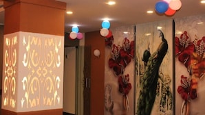 Una habitación con un muro decorativo que muestra un pavo real y arreglos florales, un pilar con patrones iluminados y un techo adornado con globos.