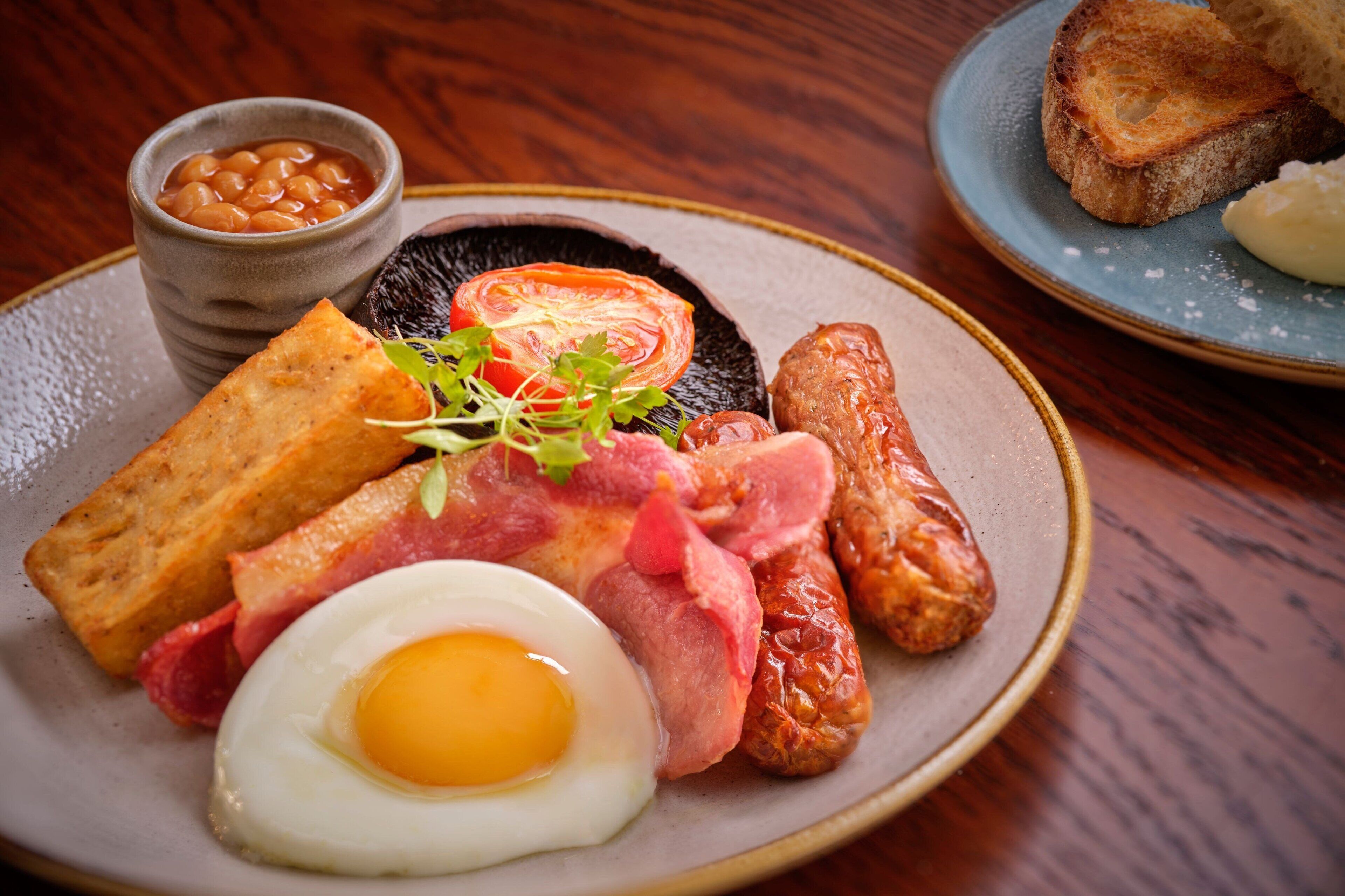 Ein Teller Frühstück mit Eiern, Speck, Würstchen, Toast und Bohnen.