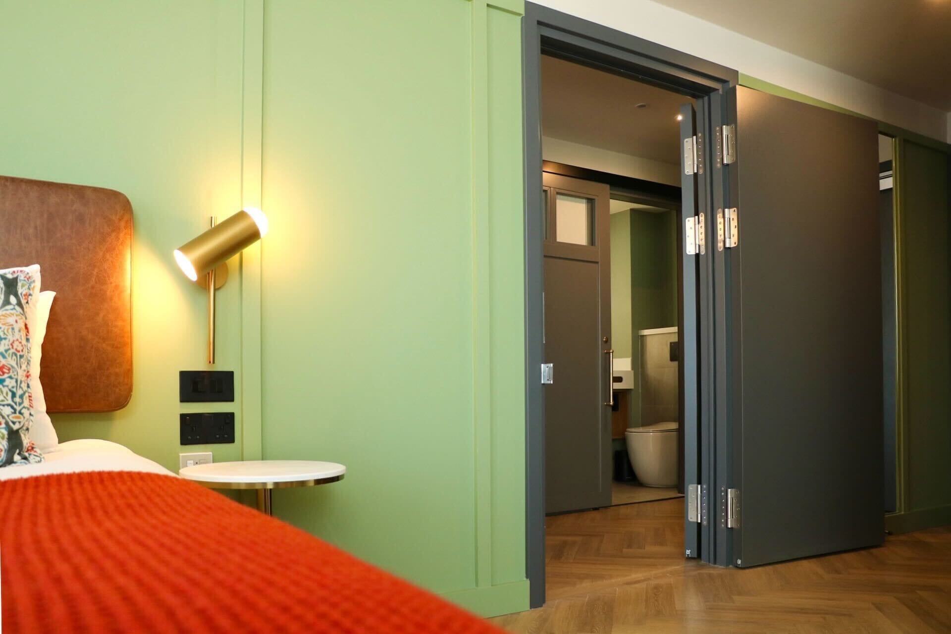 A hotel room with a bed, bedside lamp, and a view into the bathroom.