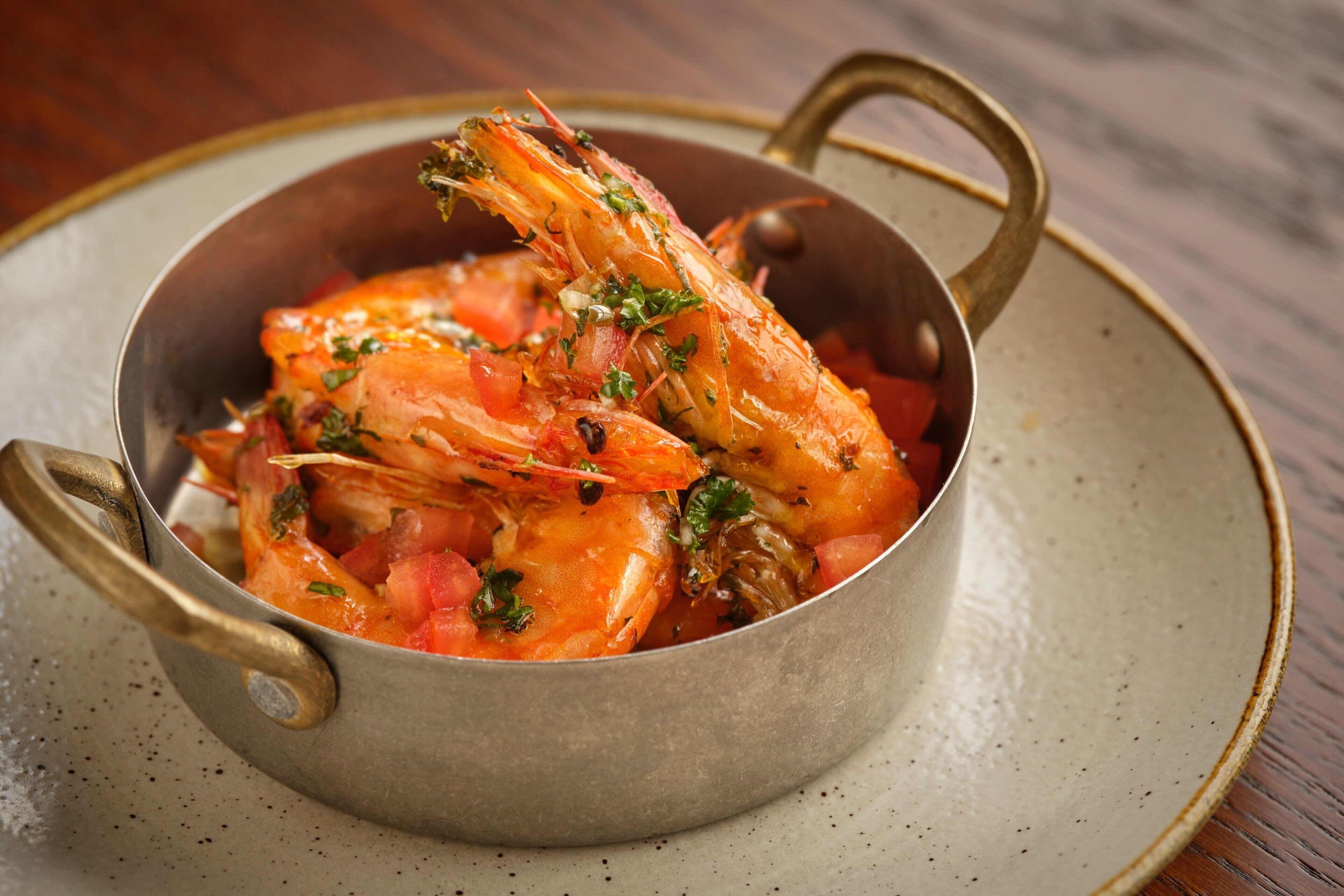 A bowl of cooked shrimp with herbs and tomatoes.