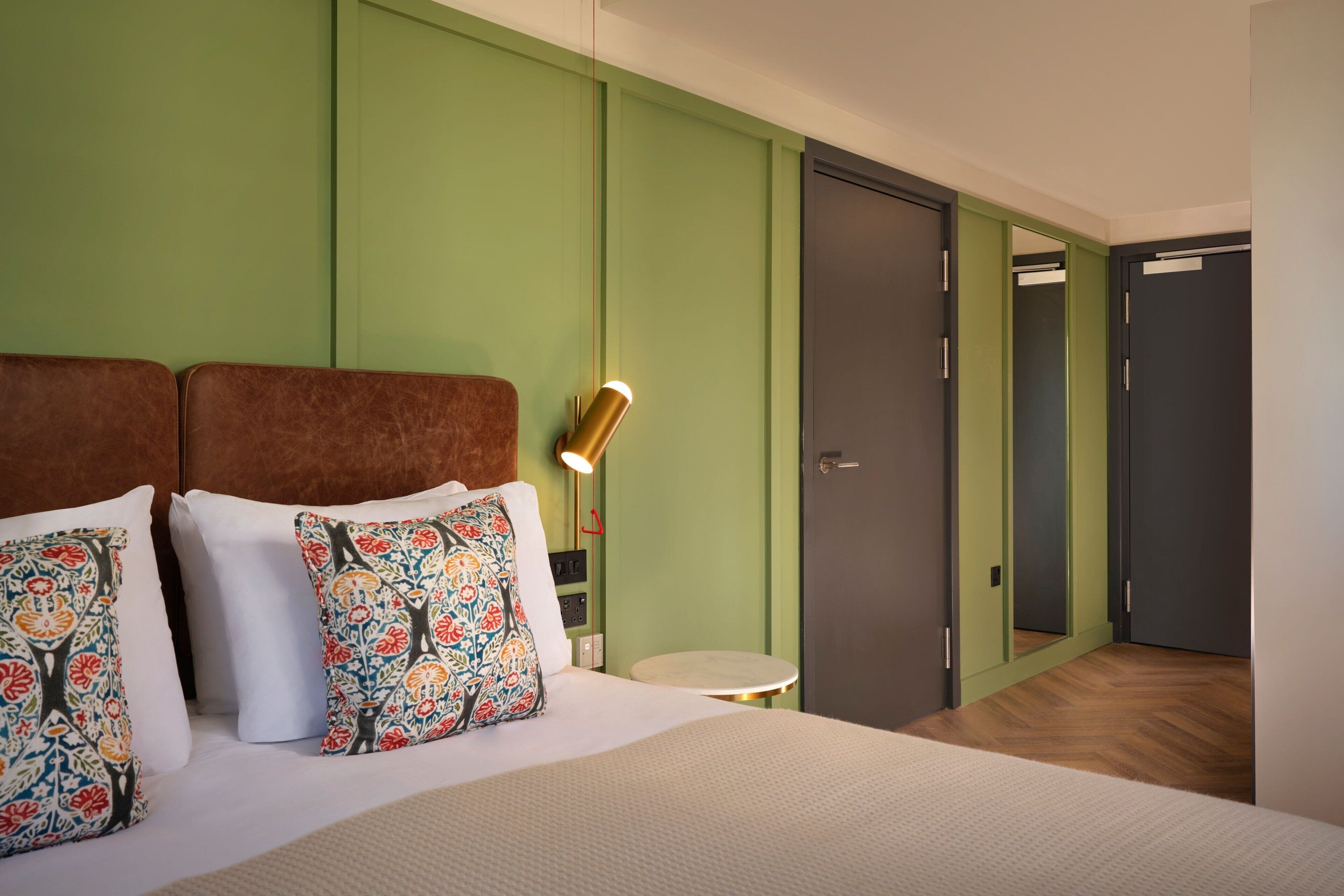 A hotel room with a bed, a bedside table, a lamp, and a mirror.