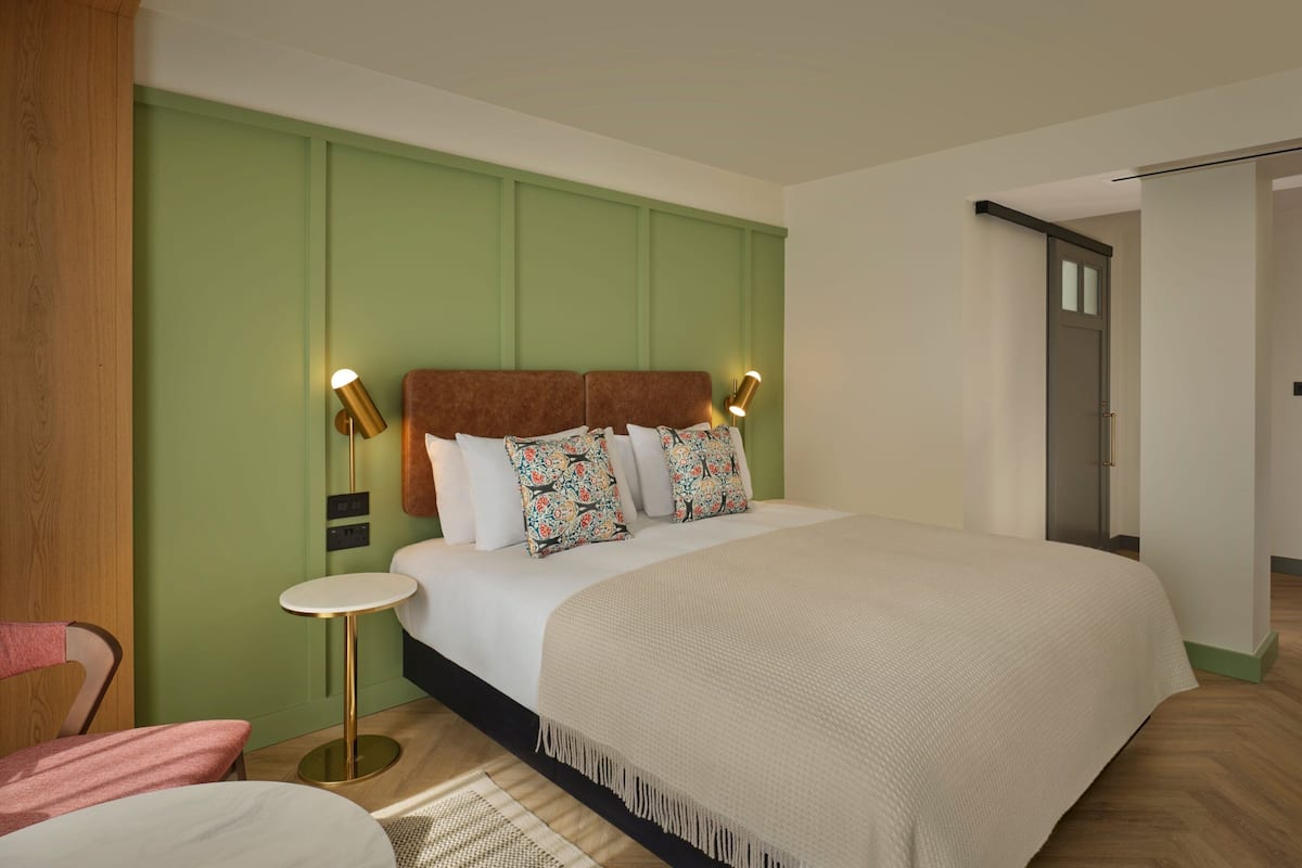 A modern hotel room with a large bed, two bedside lamps, a small round table, and a wooden chair.