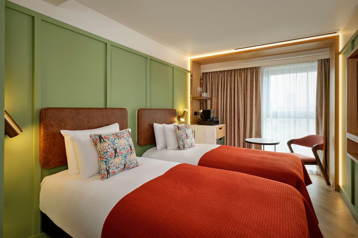 A hotel room with two beds, a desk, a chair, and a window with curtains.