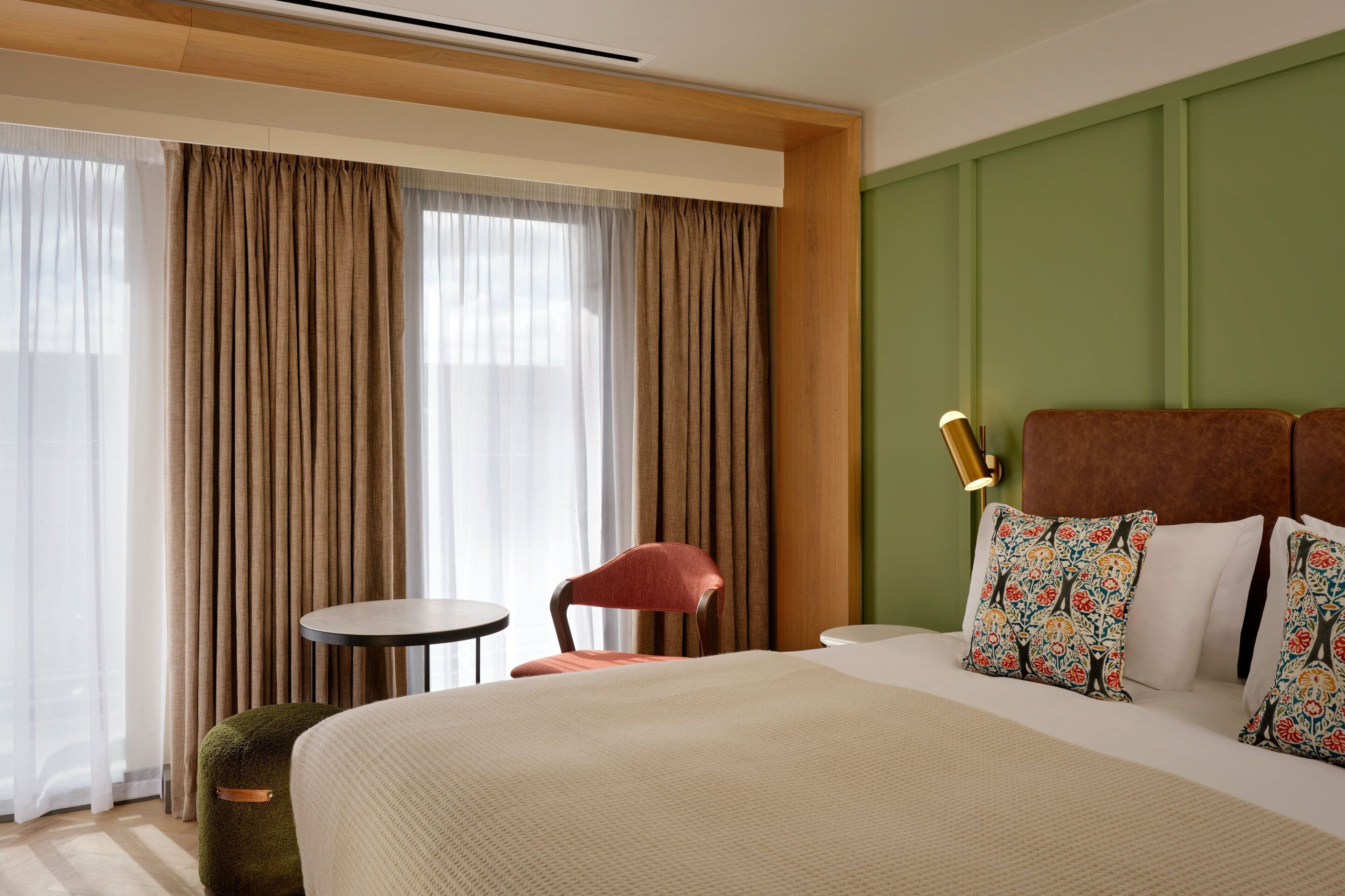 A hotel room with a large bed, a round table, a chair, and a green accent wall.