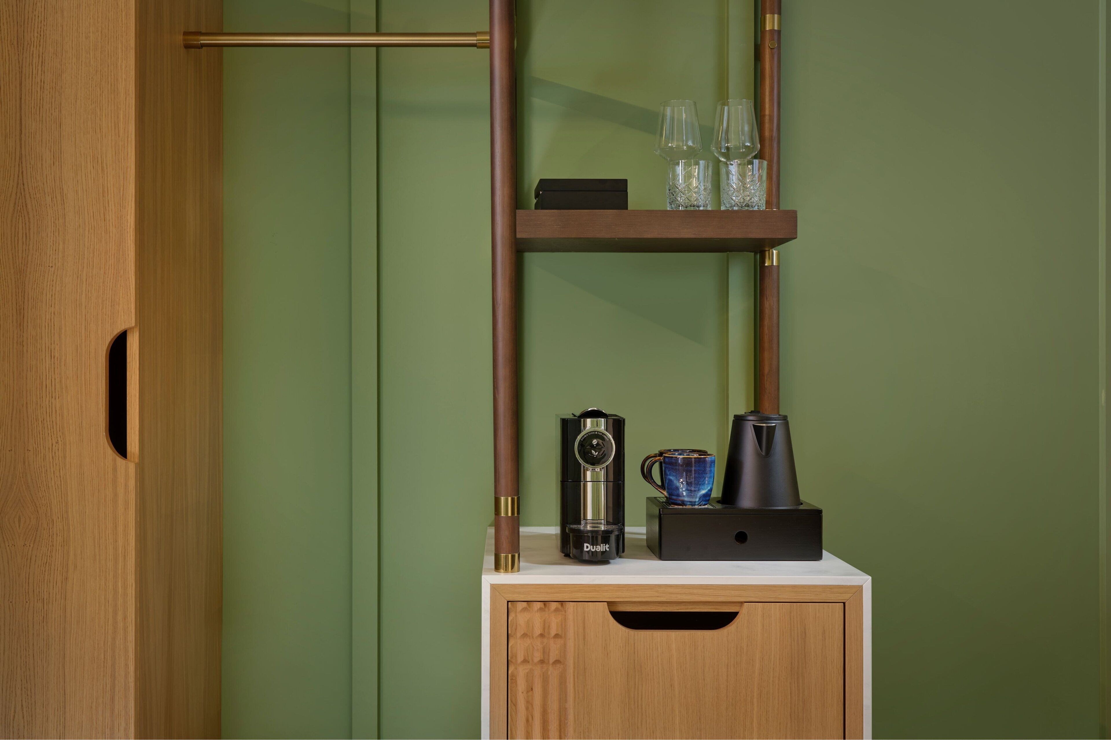 A wooden cabinet with a coffee maker, a glass, and a book on a white countertop.