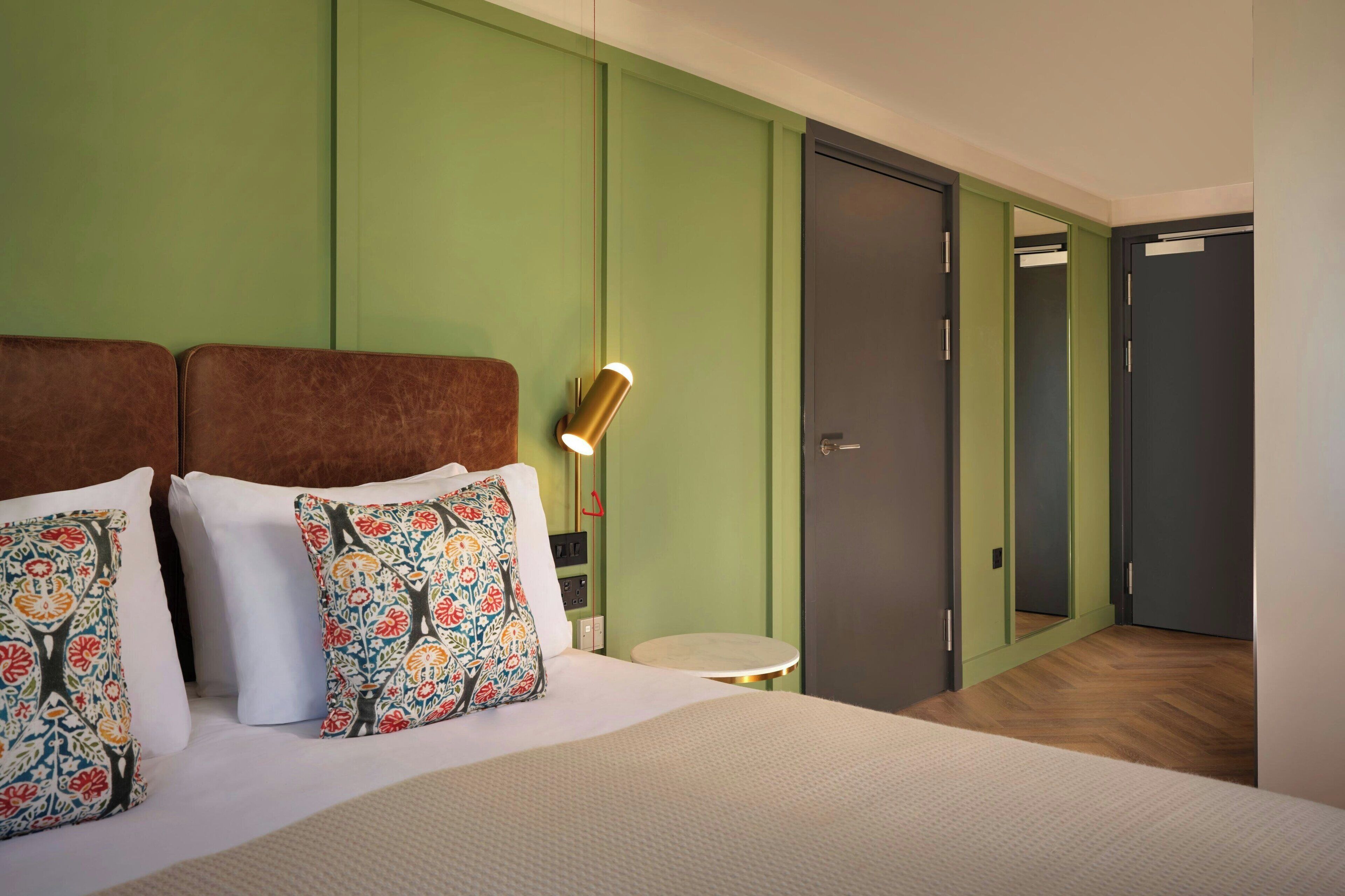 A hotel room with a bed, green walls, a round table, and a mirror.