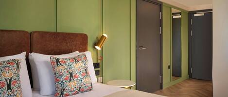 A hotel room with a bed, green walls, a round table, and a mirror.
