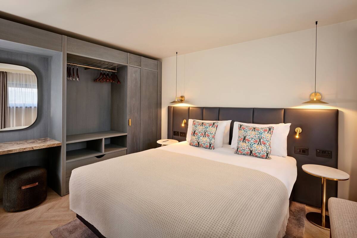 A modern bedroom with a large bed, a built-in wardrobe, a bedside table, and a small round table.