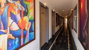 Un pasillo de hotel con puertas y un cuadro grande y colorido en la pared izquierda.
