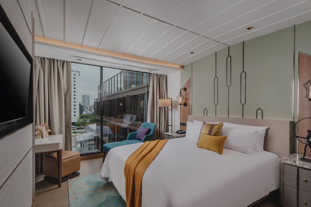 Een hotelkamer met een groot bed, een bureau, een stoel, een televisie en uitzicht op de stad.
