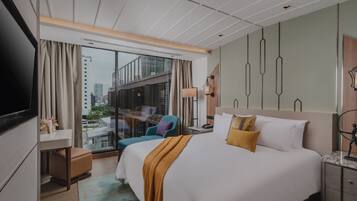 A hotel room with a large bed, a desk, a chair, a TV, and a view of the city through the window.