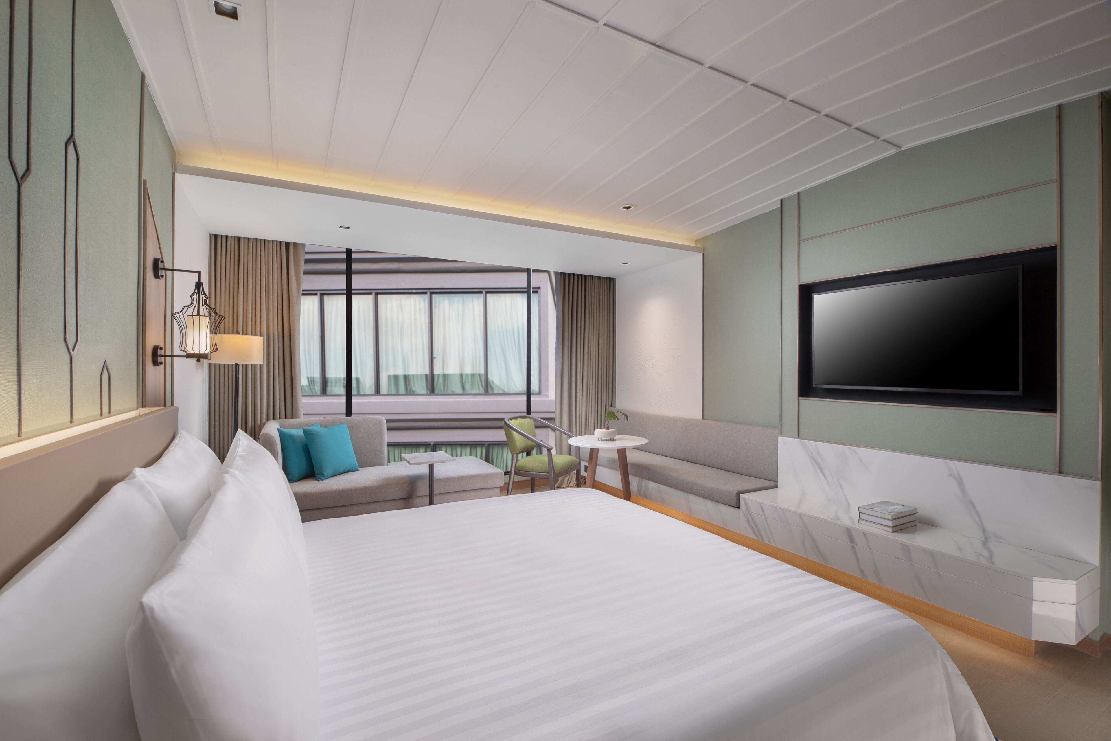 Een moderne hotelkamer met een groot bed, een bank, een klein tafeltje en een aan de muur bevestigde televisie.