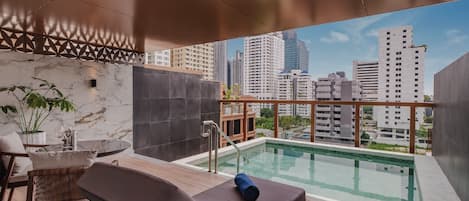 A rooftop pool area with lounge chairs, a small table, and a view of surrounding high-rise buildings.
