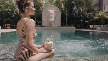 Guests can enjoy a refreshing drink by the pool surrounded by lush gardens and a unique elephant sculpture.