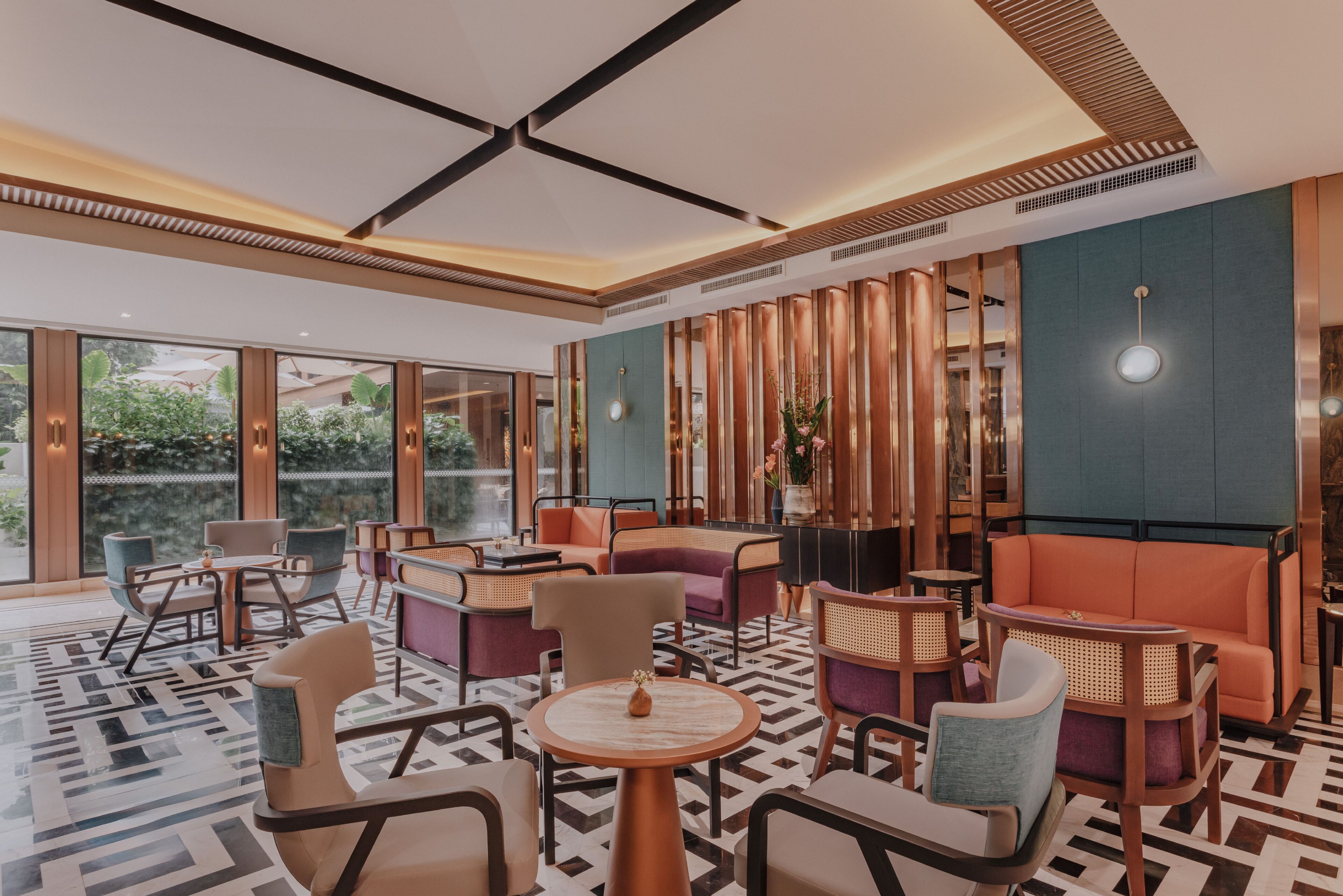 A modern lounge area with round tables and cushioned seating, large windows offering views of greenery, and a patterned floor.
