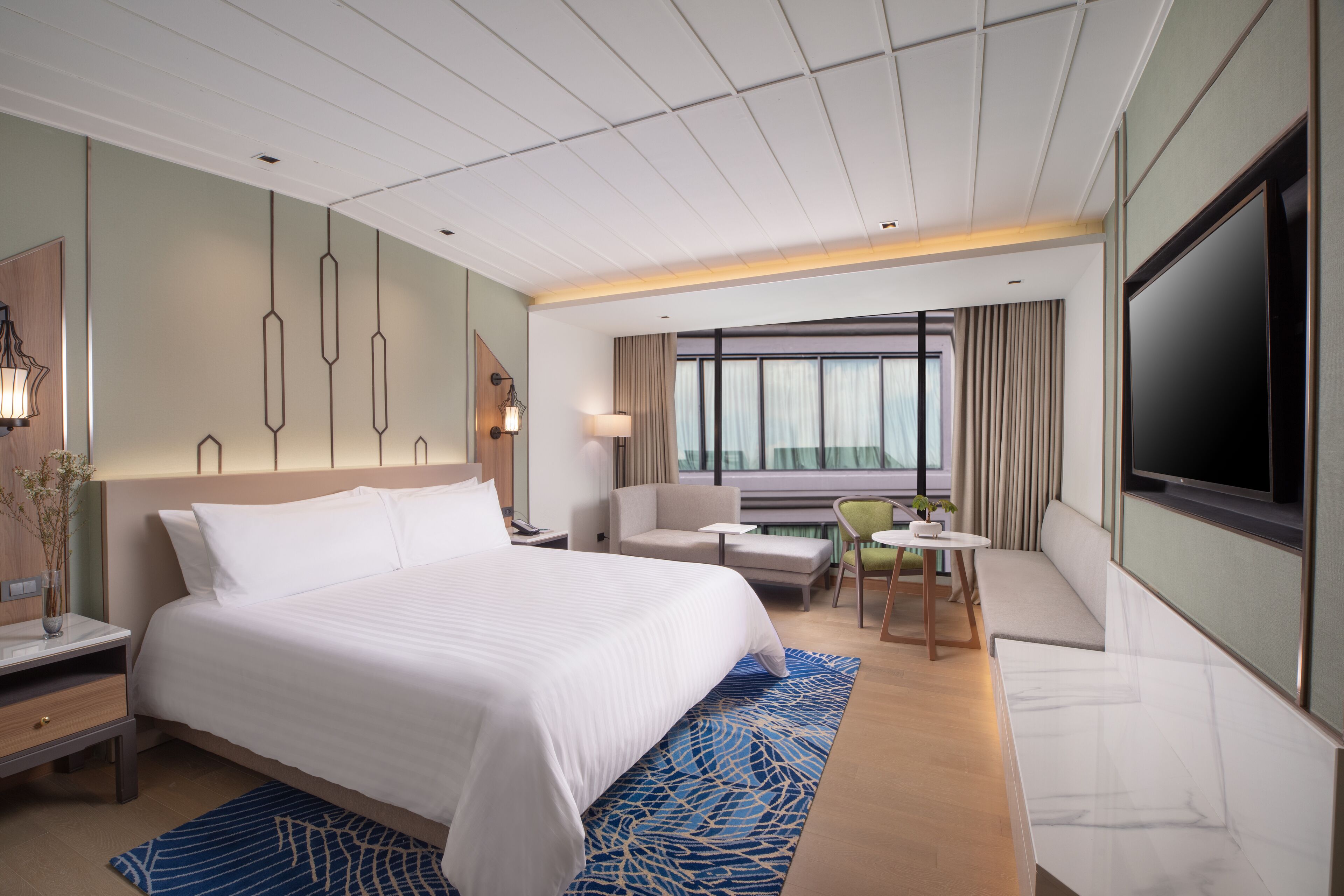A hotel room with a large bed, a TV, a desk, a chair, and a sofa.