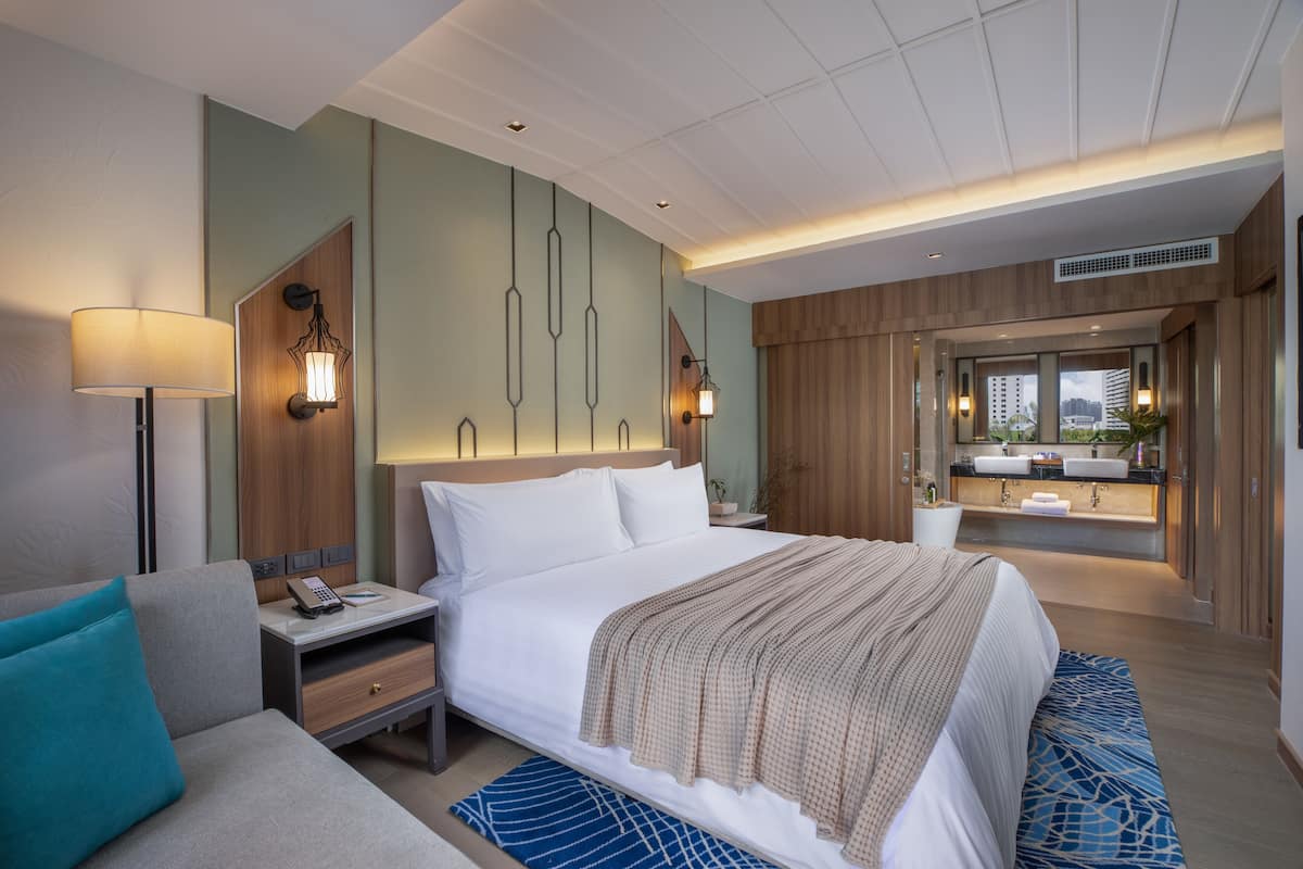 Een moderne hotelkamer met een groot bed, nachtkastjes, een bureau, een bank en een badkamer met een wastafel en spiegel.