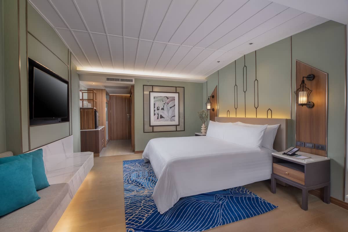 Een moderne hotelkamer met een groot bed, een flatscreen televisie, een nachtkastje met een lamp en een houten garderobe.