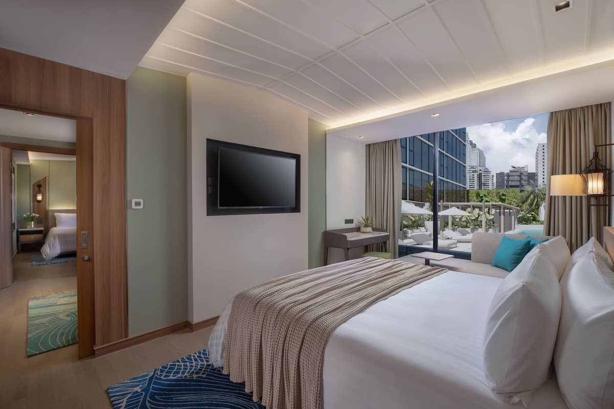 Een hotelkamer met een groot bed, een flatscreen televisie, een bureau met een stoel, en uitzicht op de stad door grote ramen.