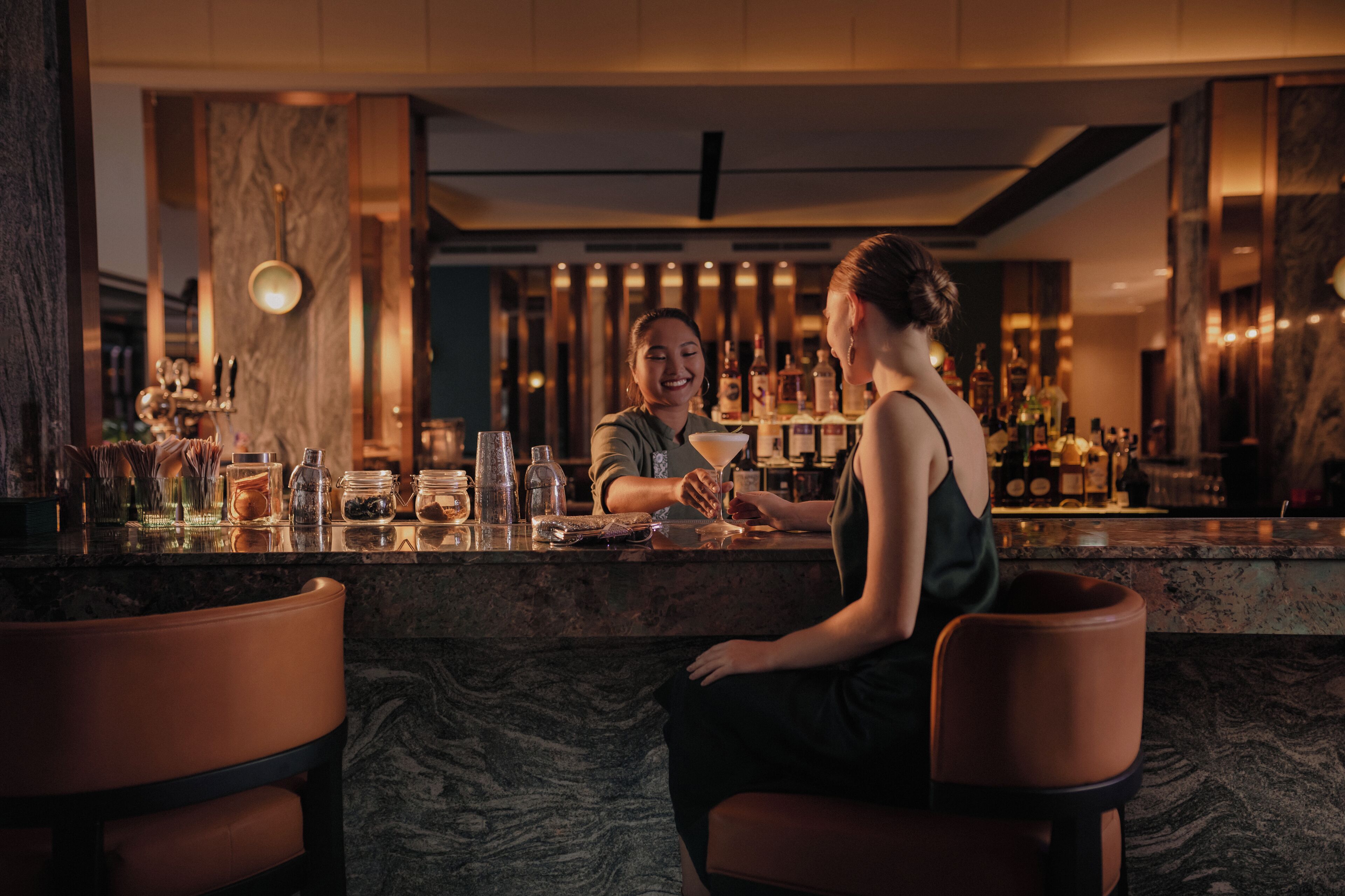 A bar area with marble countertops, bar stools, and a variety of bottles and glasses.