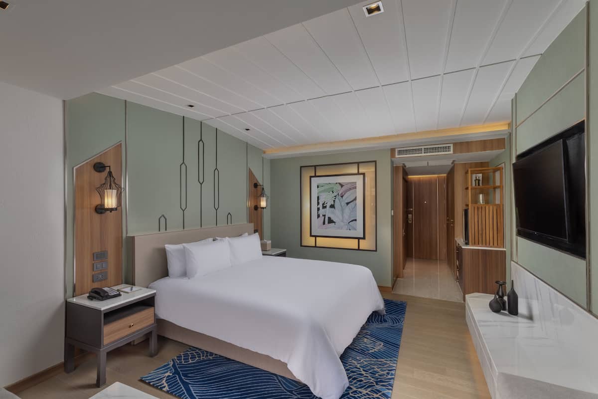 Een hotelkamer met een groot bed, nachtkastje, een tv aan de muur en een schilderij.