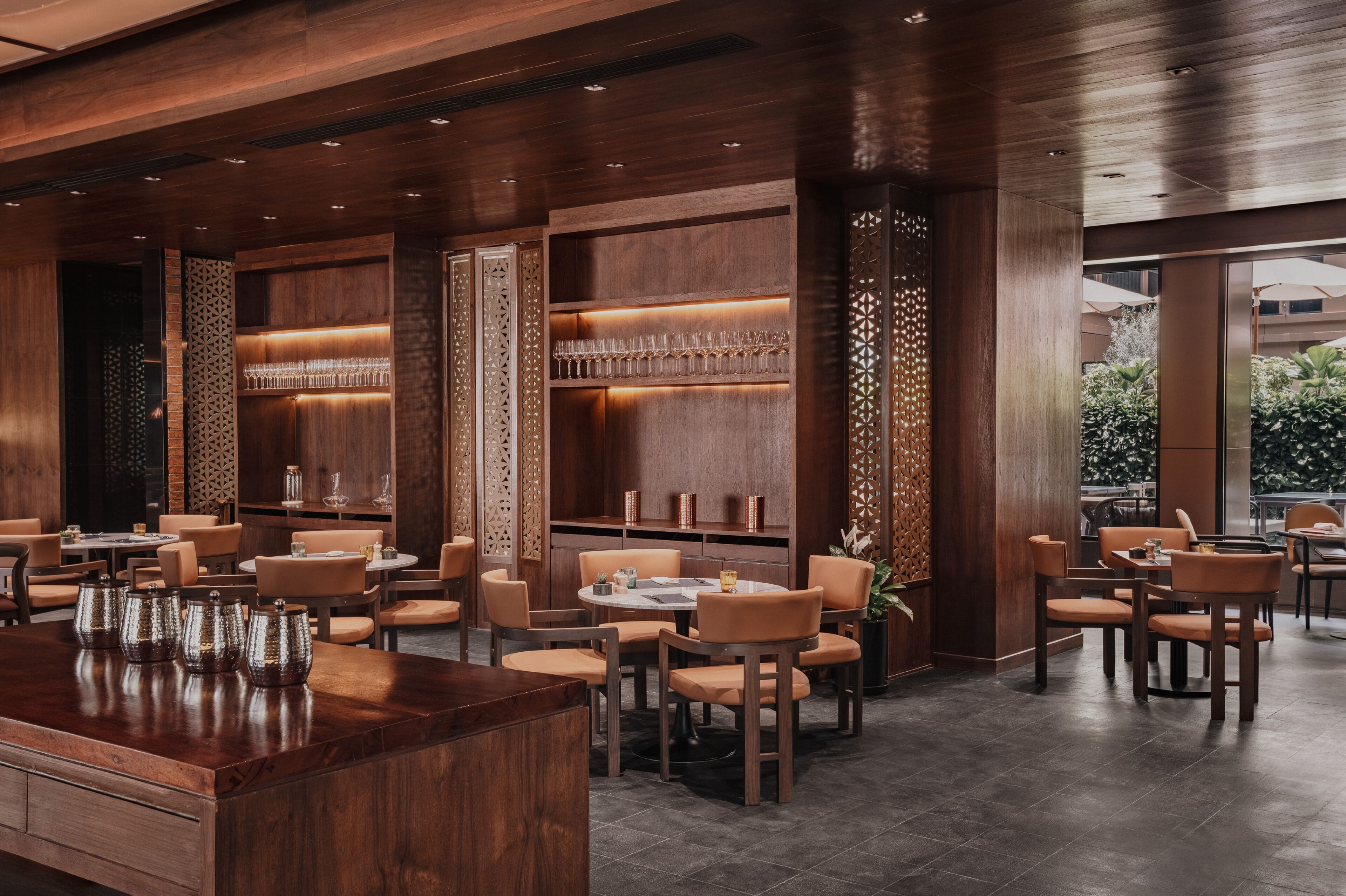 A modern restaurant interior with wooden paneling, round tables, and orange chairs.