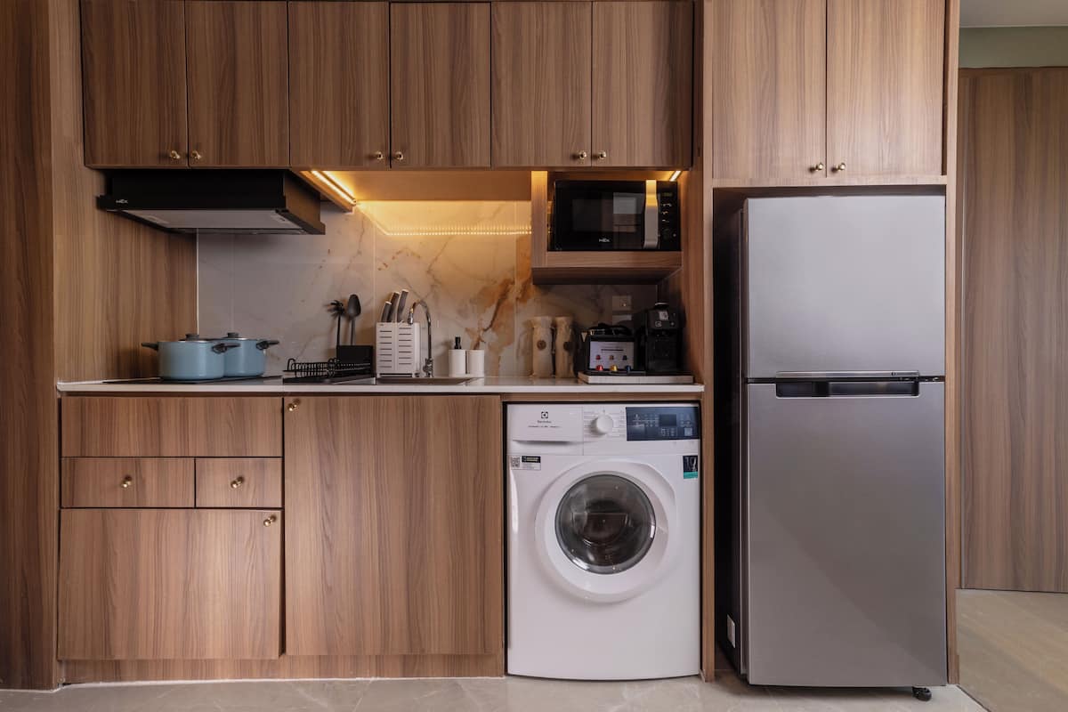 Een moderne keuken met houten kastjes, een ingebouwde wasmachine, een magnetron en een koelkast.