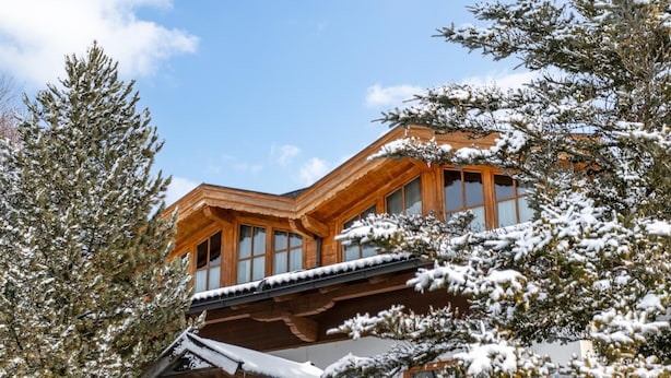 Una cabaña de madera con ventanas amplias y techo inclinado, rodeada de árboles cubiertos de nieve.