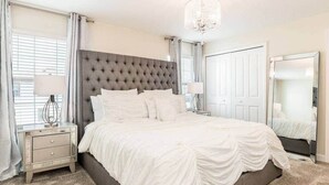 Quarto com cabeceira estofada, cama grande, mesa de cabeceira com abajur, cômoda e espelho.