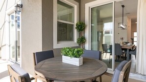 Een ronde houten tafel met stoelen, een potplant en een raam met jaloezieën.