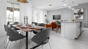 Ett modernt kök med en central köksö, en matplats med stolar och en tv som är monterad på väggen.