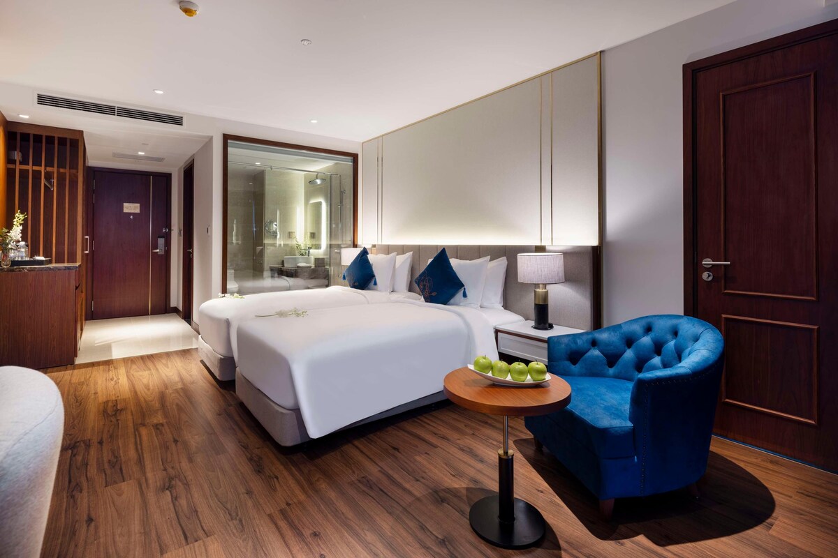 A hotel room with a large bed, bedside table, and a blue armchair.