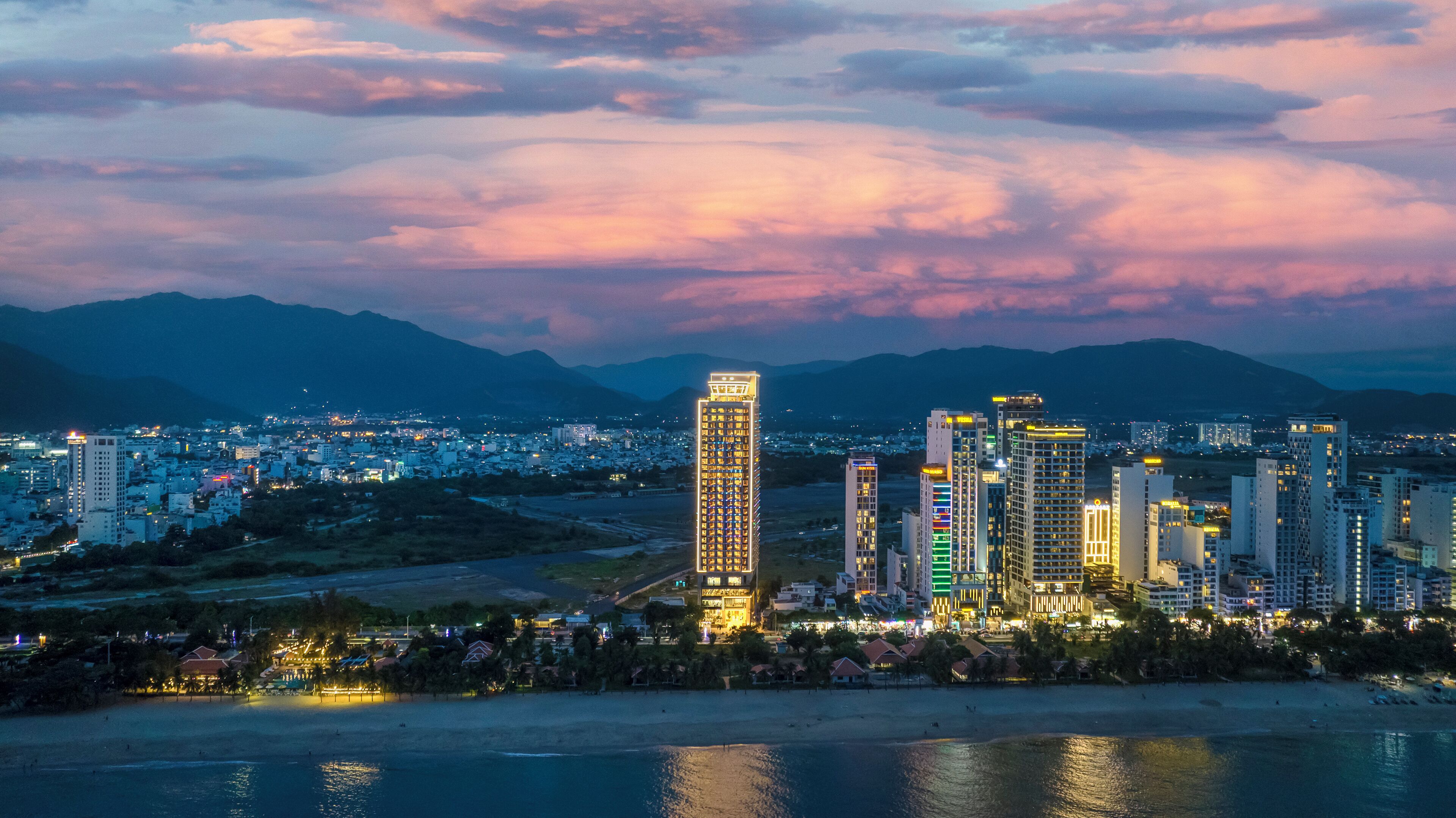 Un paisaje urbano con rascacielos, una playa y montañas al fondo.