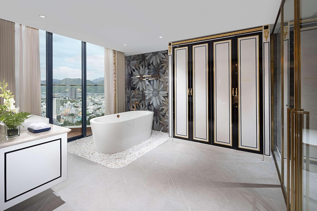 A modern bathroom with a freestanding bathtub, a large mirror, and a view of a cityscape through floor-to-ceiling windows.