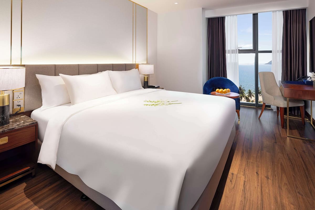 A hotel room with a large bed, a desk, and a view of the sea.