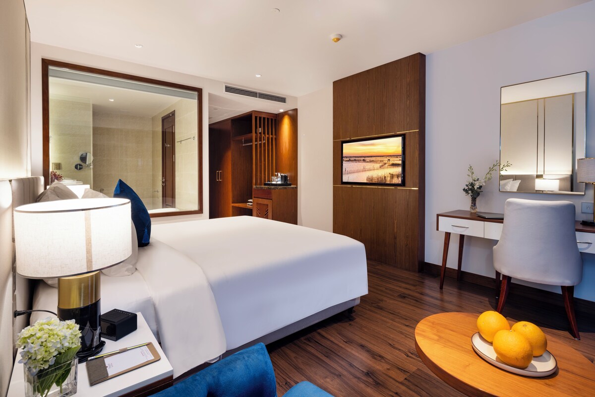A hotel room with a large bed, a desk, a chair, and a television.