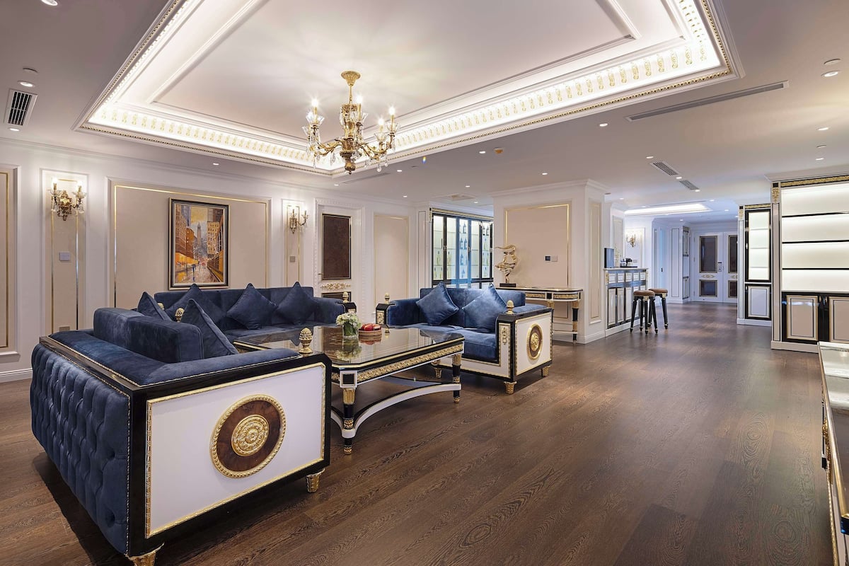 A luxurious living room with two blue sofas, a glass coffee table, and a chandelier.