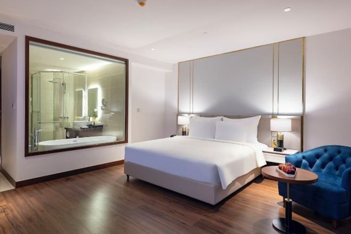Une chambre d’hôtel moderne avec un grand lit, une douche en verre, une table ronde et un fauteuil bleu.