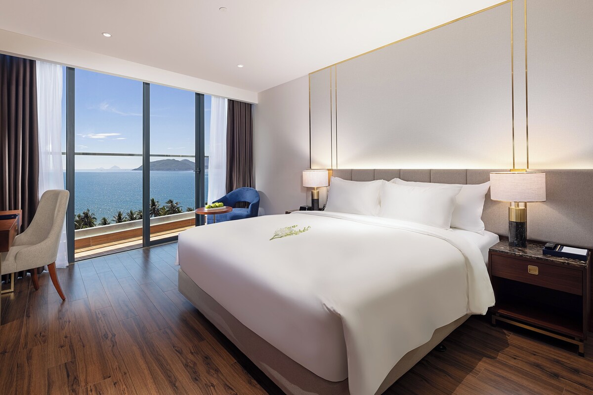 Une chambre d’hôtel spacieuse, dotée d’un grand lit, d’un bureau et d’une chaise. La chambre offre une vue sur la mer et les montagnes.