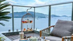 A balcony with a table set for a meal, a chair, a birdcage with snacks, and a view of the sea and mountains. - Best Western Premier Marvella Nha Trang (Nha Trang)