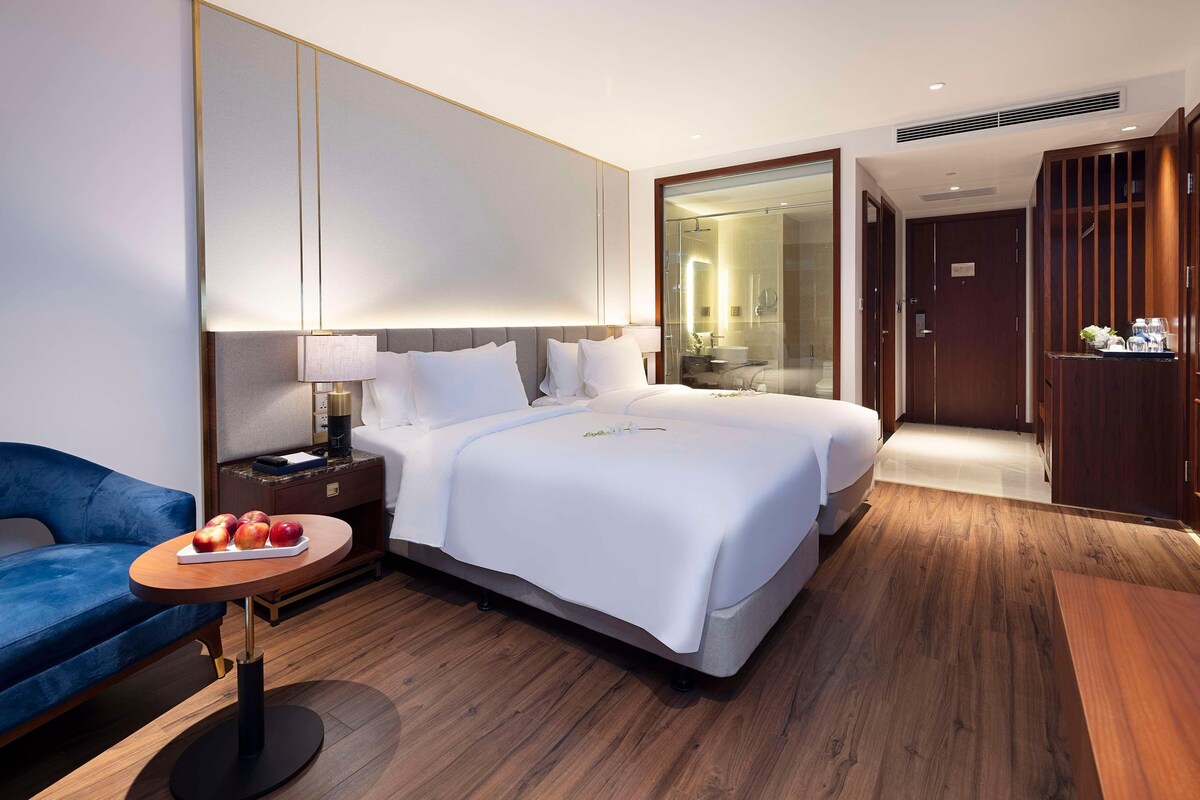 A hotel room with a bed, bedside table, lamp, and a small round table with fruit.