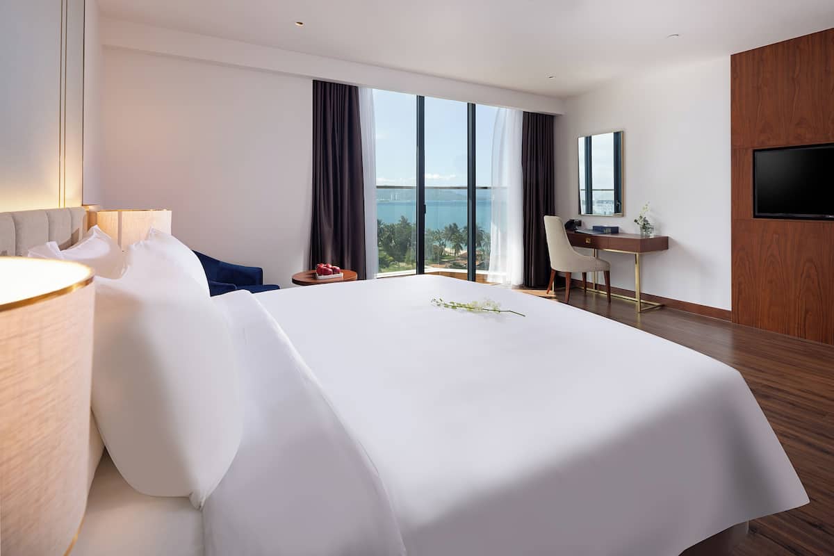 A hotel room with a large bed, a desk, a TV, and a view of the ocean.