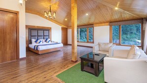 A spacious bedroom with a large bed, a sitting area with a sofa, and a view of the outdoors through large windows. - DLS Serenity Resort And Spa (Manali)