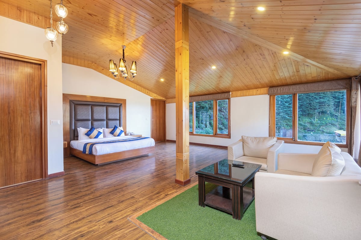 Ein großzügiges Schlafzimmer mit einem großen Bett, einer Sitzecke mit einer Couch und Blick ins Freie durch große Fenster.