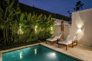 A poolside area with two lounge chairs, a small table, and a wall-mounted light fixture. - Villa Isola Gallinara (Canggu)