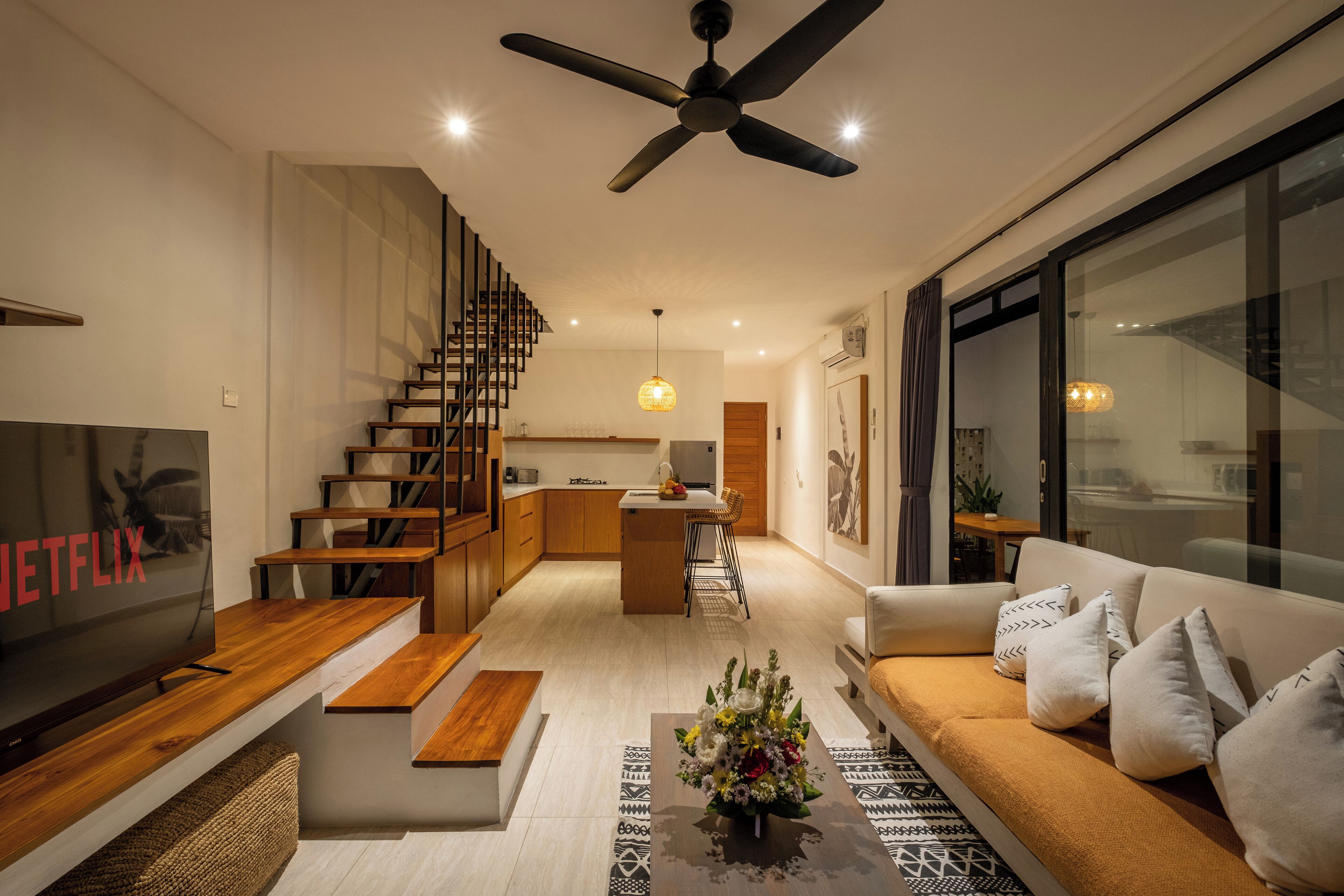 A modern living room with a TV, sofa, coffee table, and staircase leading to a kitchen.