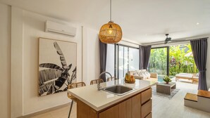 Una cocina moderna con una isla central, una zona de comedor con sillas, un ventanal con cortinas y un ventilador de techo.
