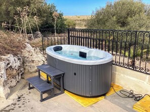A hot tub with a bench, surrounded by a metal fence, set against a natural landscape. - Pleasant Stone House & Jacuzzi St Martin (Mgarr)