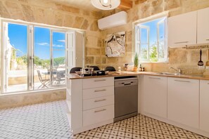 A kitchen with stone walls, white cabinets, a dishwasher, and a large window.